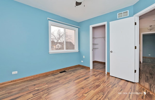 unfurnished bedroom featuring a spacious closet, hardwood / wood-style floors, ceiling fan, and a closet