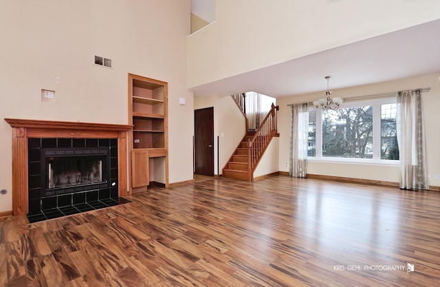 unfurnished living room with hardwood / wood-style flooring, an inviting chandelier, a fireplace, and built in shelves