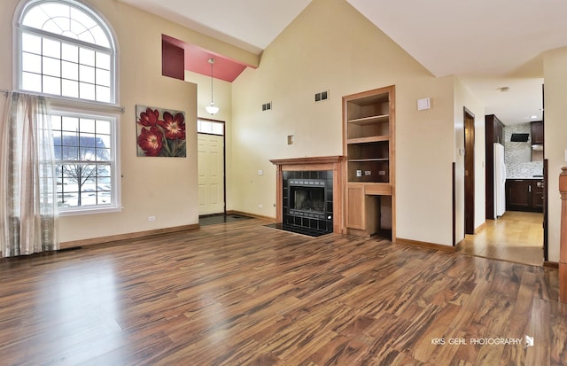 unfurnished living room with a high ceiling, a tile fireplace, hardwood / wood-style flooring, and built in features