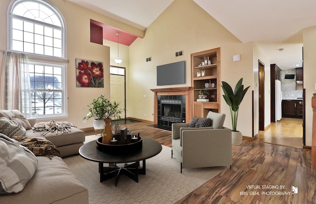 living room with a high ceiling, a tile fireplace, hardwood / wood-style flooring, and built in shelves