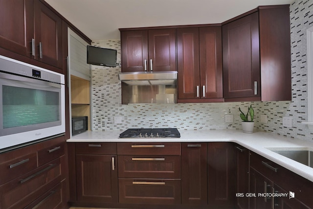 kitchen with stainless steel gas stovetop, sink, white oven, and backsplash