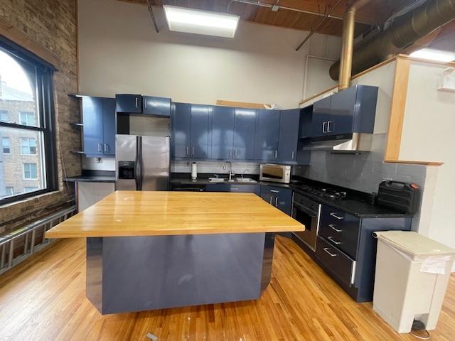 kitchen featuring sink, stainless steel appliances, a high ceiling, blue cabinets, and light wood-type flooring