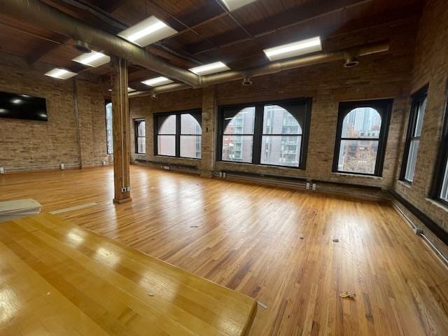 spare room featuring brick wall and light wood-type flooring