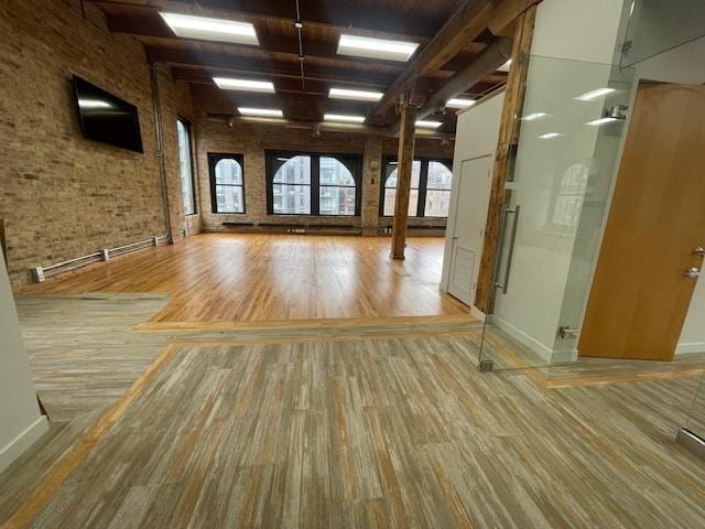 empty room featuring a baseboard radiator, brick wall, and hardwood / wood-style floors