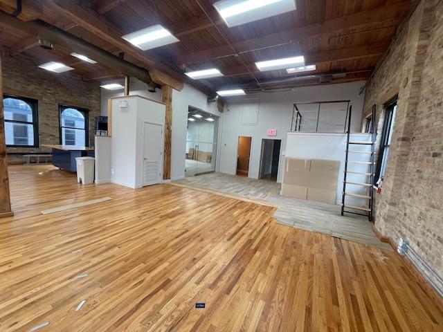 unfurnished room with brick wall, a healthy amount of sunlight, and light hardwood / wood-style flooring