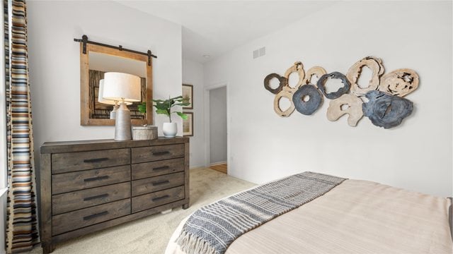 bedroom with a barn door and light carpet