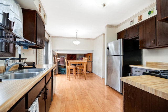 kitchen featuring pendant lighting, a sink, light wood-style floors, freestanding refrigerator, and crown molding