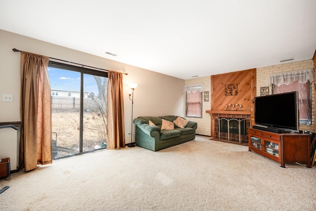 living room featuring visible vents, an accent wall, wood walls, carpet floors, and a brick fireplace