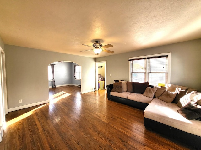 living room with a textured ceiling, dark wood-type flooring, and ceiling fan