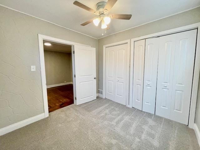 unfurnished bedroom with light carpet, two closets, and ceiling fan