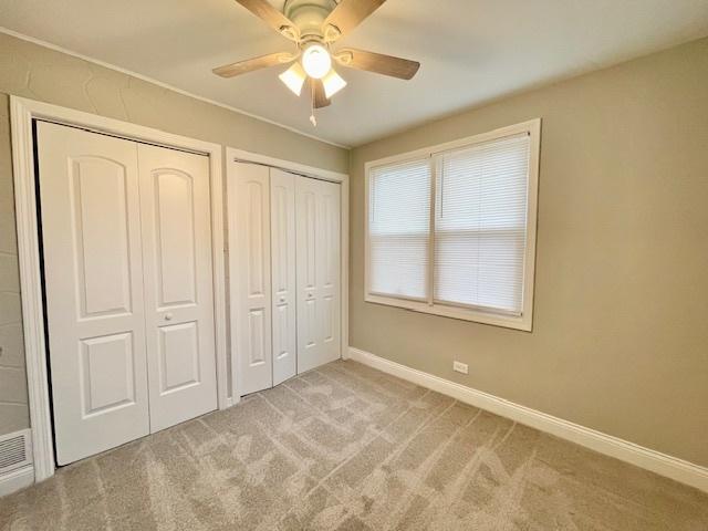 unfurnished bedroom with multiple closets, light colored carpet, and ceiling fan