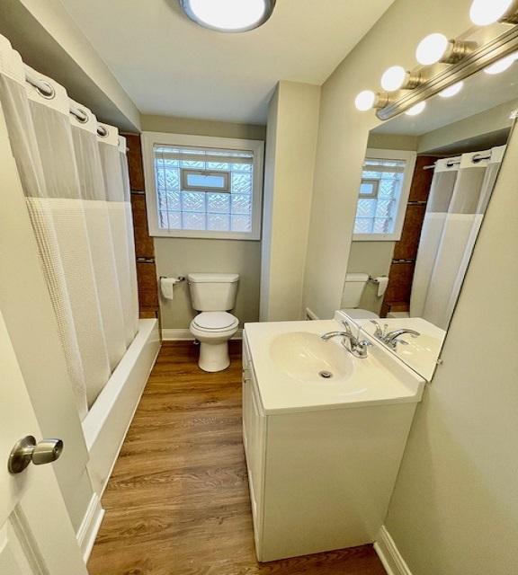 full bathroom featuring wood-type flooring, vanity, shower / bath combo with shower curtain, and toilet