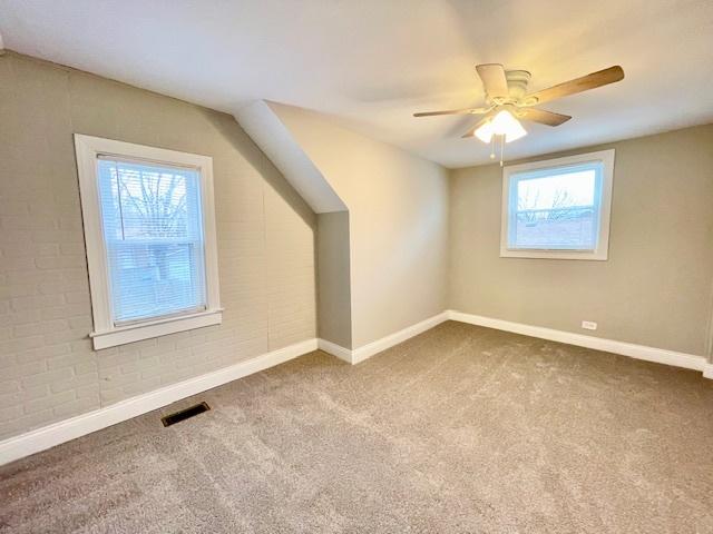 additional living space with carpet floors, a healthy amount of sunlight, and brick wall