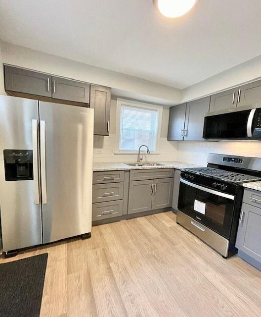 kitchen with gray cabinets, sink, backsplash, stainless steel appliances, and light hardwood / wood-style flooring