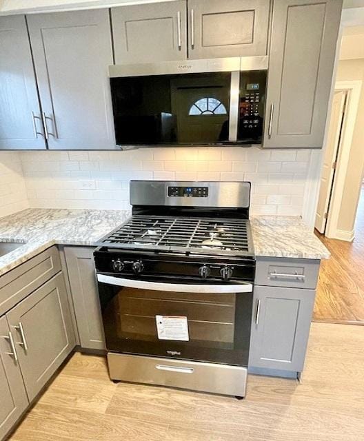 kitchen featuring gray cabinets, appliances with stainless steel finishes, backsplash, light stone counters, and light wood-type flooring