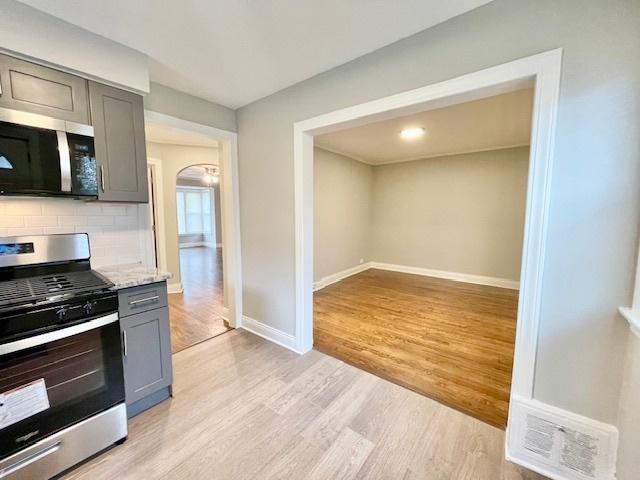 kitchen with gray cabinets, backsplash, light stone counters, stainless steel appliances, and light wood-type flooring