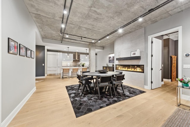 dining area with track lighting, a tile fireplace, and light wood-type flooring