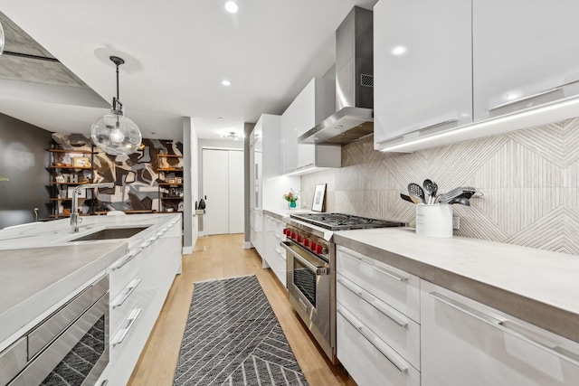 kitchen featuring appliances with stainless steel finishes, white cabinetry, sink, hanging light fixtures, and wall chimney exhaust hood