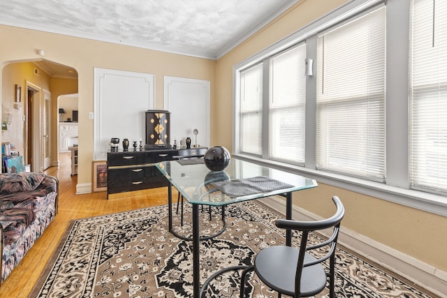 office featuring light wood-type flooring, plenty of natural light, arched walkways, and ornamental molding