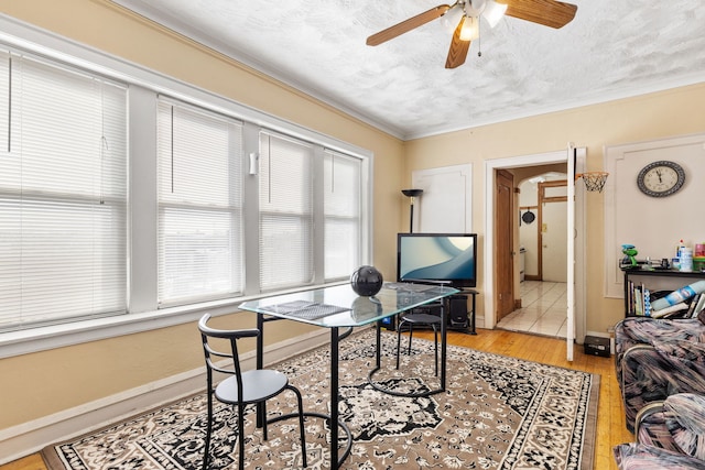 office area with a ceiling fan, baseboards, light wood-style flooring, a textured ceiling, and crown molding