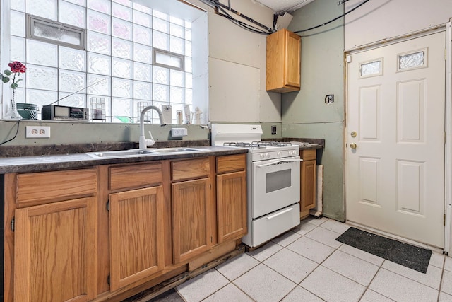 kitchen featuring white range with gas stovetop, light tile patterned flooring, a sink, dark countertops, and brown cabinets