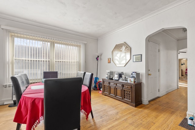 dining room with light wood-type flooring, arched walkways, and crown molding