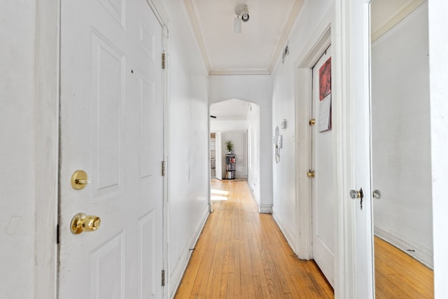 hallway with arched walkways, light wood-type flooring, crown molding, and baseboards