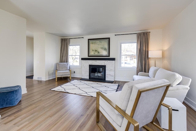 living area with a stone fireplace, baseboards, and wood finished floors