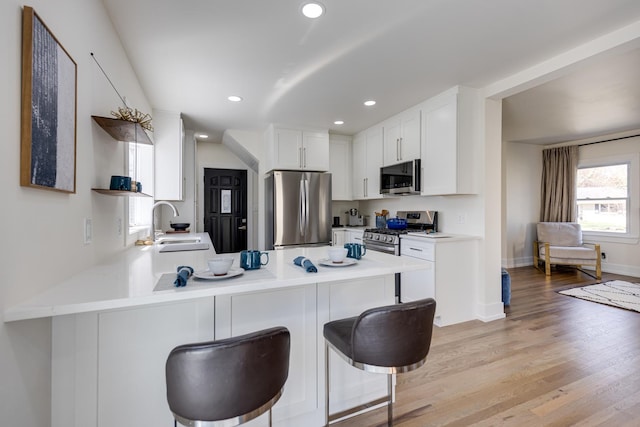 kitchen with open shelves, light countertops, appliances with stainless steel finishes, light wood-style floors, and a peninsula