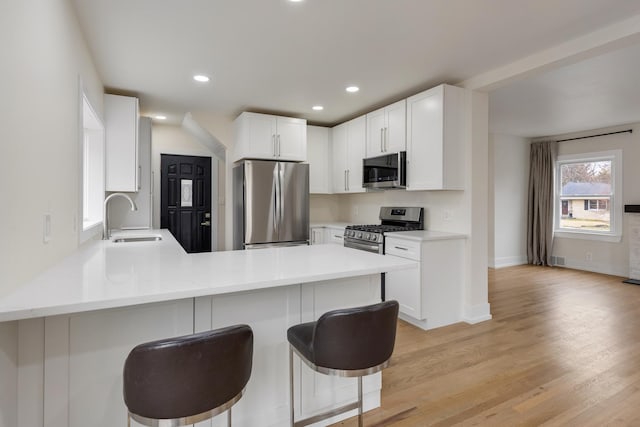 kitchen with a kitchen bar, a peninsula, a sink, light countertops, and stainless steel appliances