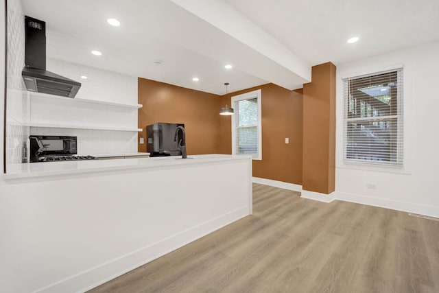 kitchen with pendant lighting, sink, kitchen peninsula, wall chimney exhaust hood, and light wood-type flooring