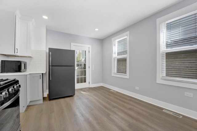 kitchen with tasteful backsplash, fridge, range with gas stovetop, light hardwood / wood-style floors, and white cabinets