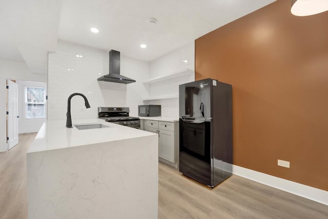 kitchen featuring black appliances, sink, light hardwood / wood-style floors, kitchen peninsula, and wall chimney range hood