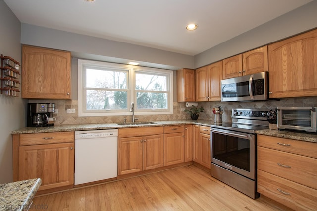 kitchen featuring appliances with stainless steel finishes, sink, decorative backsplash, light stone countertops, and light wood-type flooring