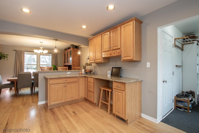 kitchen featuring decorative light fixtures, light wood-type flooring, kitchen peninsula, light stone countertops, and an inviting chandelier