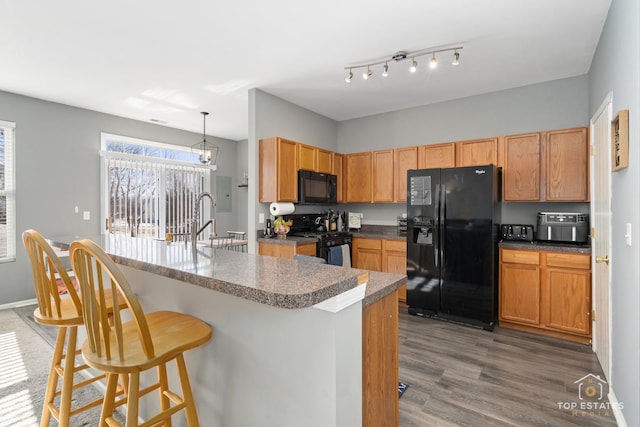 kitchen with decorative light fixtures, sink, a breakfast bar area, dark hardwood / wood-style flooring, and black appliances