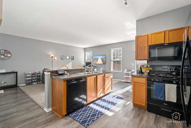 kitchen with sink, a kitchen island with sink, hardwood / wood-style floors, and black appliances