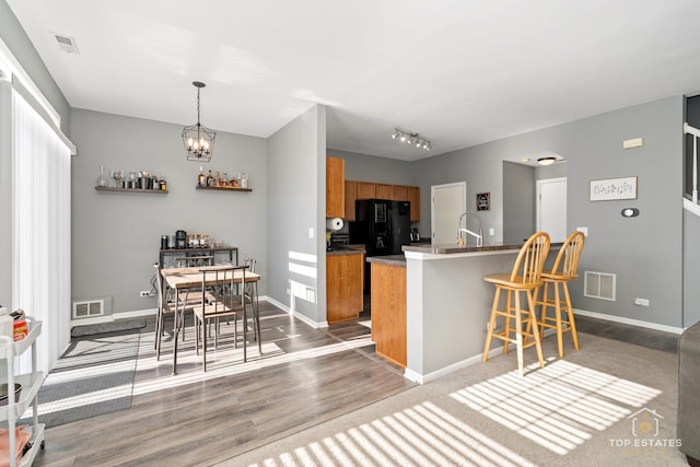 kitchen with a breakfast bar, wood-type flooring, sink, black fridge, and an inviting chandelier