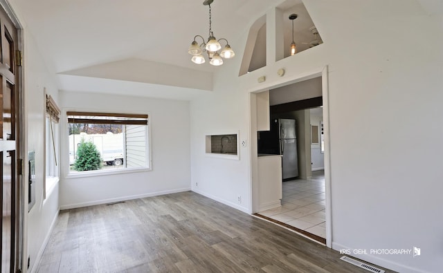 empty room with a notable chandelier, wood-type flooring, and vaulted ceiling