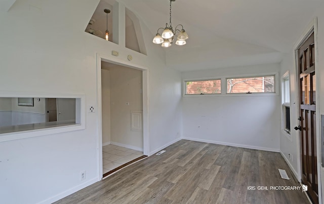 unfurnished dining area featuring a notable chandelier, wood-type flooring, and vaulted ceiling