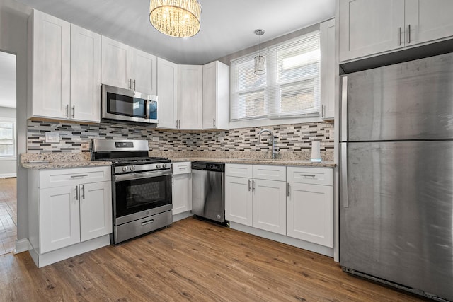 kitchen featuring appliances with stainless steel finishes, white cabinetry, backsplash, light hardwood / wood-style floors, and decorative light fixtures