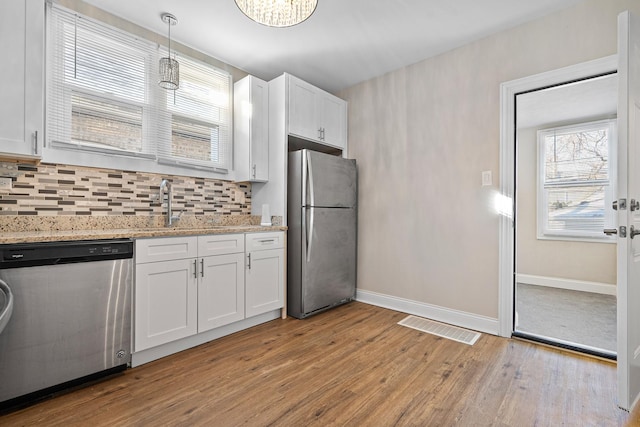 kitchen with appliances with stainless steel finishes, pendant lighting, white cabinetry, sink, and light wood-type flooring