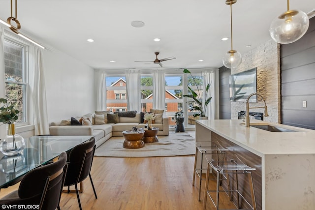 kitchen featuring an island with sink, sink, hanging light fixtures, ceiling fan, and light hardwood / wood-style flooring