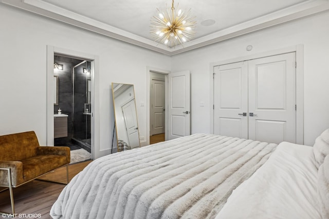 bedroom featuring ensuite bath, an inviting chandelier, wood-type flooring, a raised ceiling, and a closet