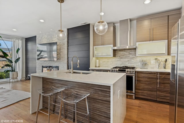 kitchen with sink, hanging light fixtures, light wood-type flooring, stainless steel appliances, and wall chimney range hood