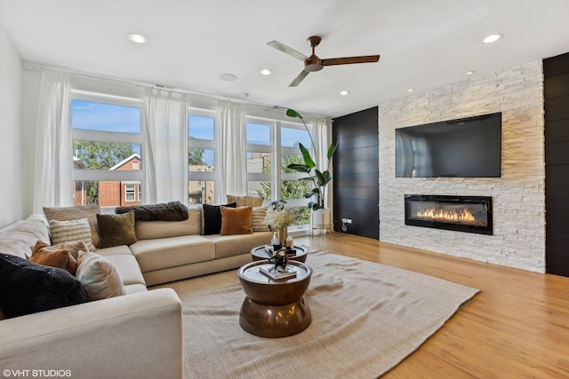 living room featuring ceiling fan, a stone fireplace, a wealth of natural light, and wood-type flooring