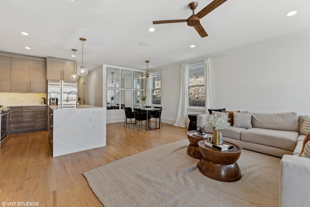 living room with sink, ceiling fan, and light wood-type flooring