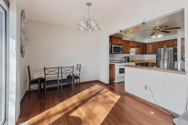 kitchen with decorative light fixtures, appliances with stainless steel finishes, brown cabinetry, dark wood-type flooring, and a sink