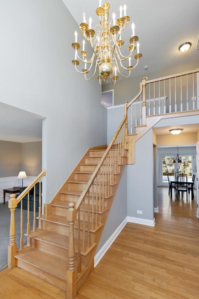 stairs featuring wood-type flooring, a chandelier, and a high ceiling