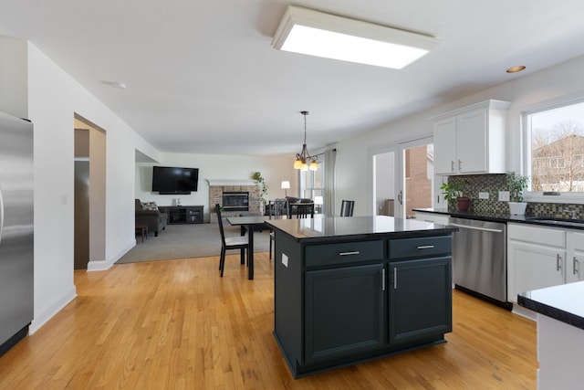 kitchen with appliances with stainless steel finishes, a center island, white cabinets, decorative light fixtures, and light wood-type flooring